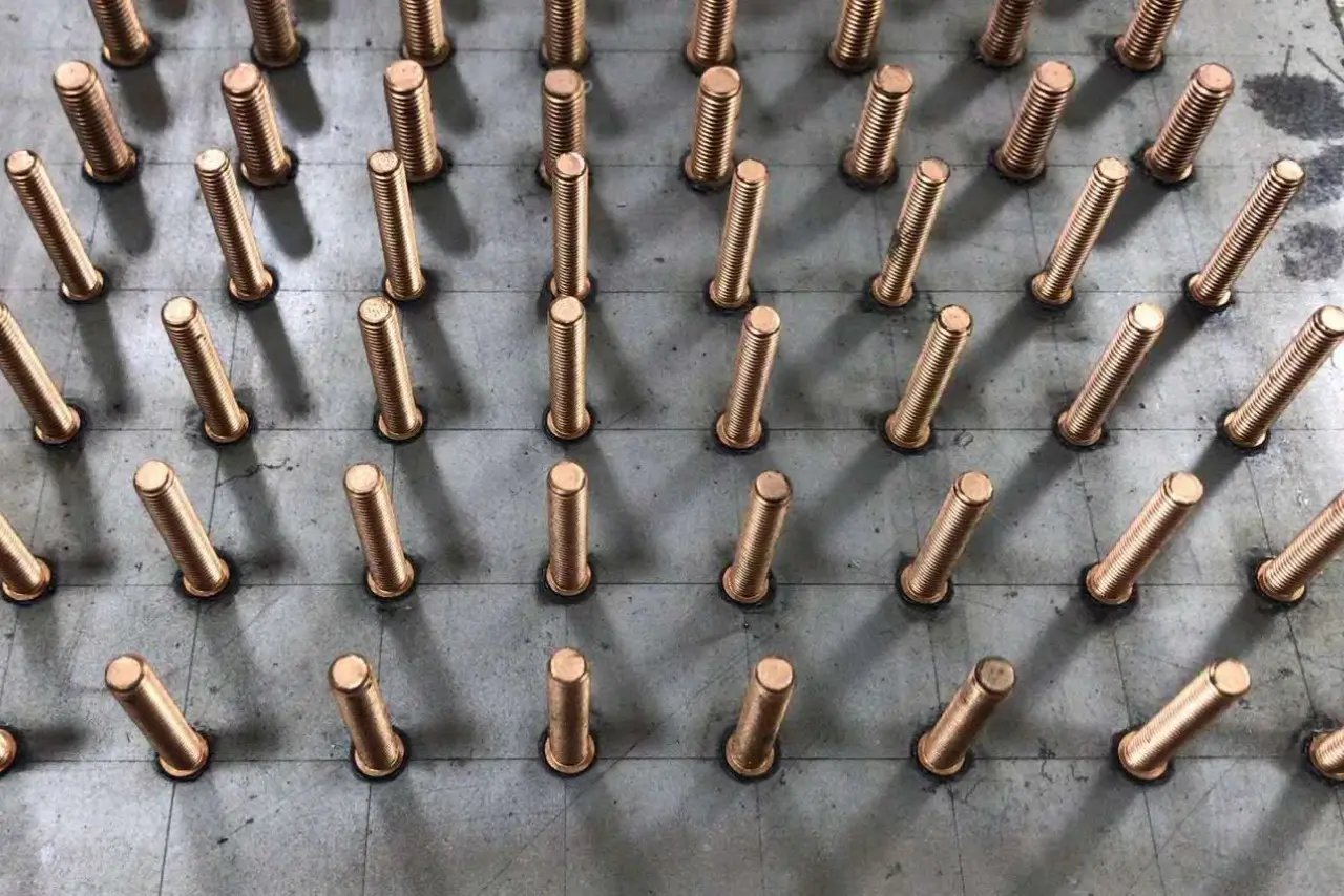 Array of precision-welded shear studs (connectors) secured to a steel structure plate in a controlled industrial stud welding workshop environment.