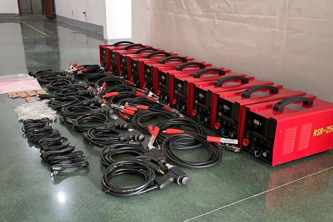 A row of industrial red RSR-2500 capacitor discharge stud welding machines with accompanying welding guns and grounding cables laid out on a workshop floor.
