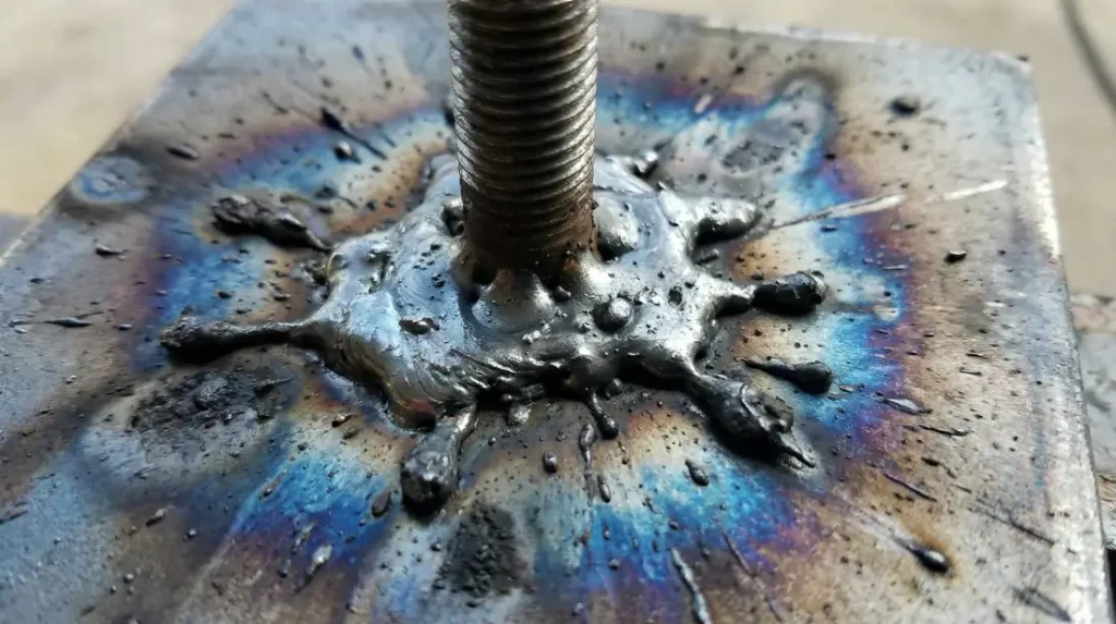 Close-up of a hot weld error in CD stud welding showing excessive molten metal splash and discoloration.