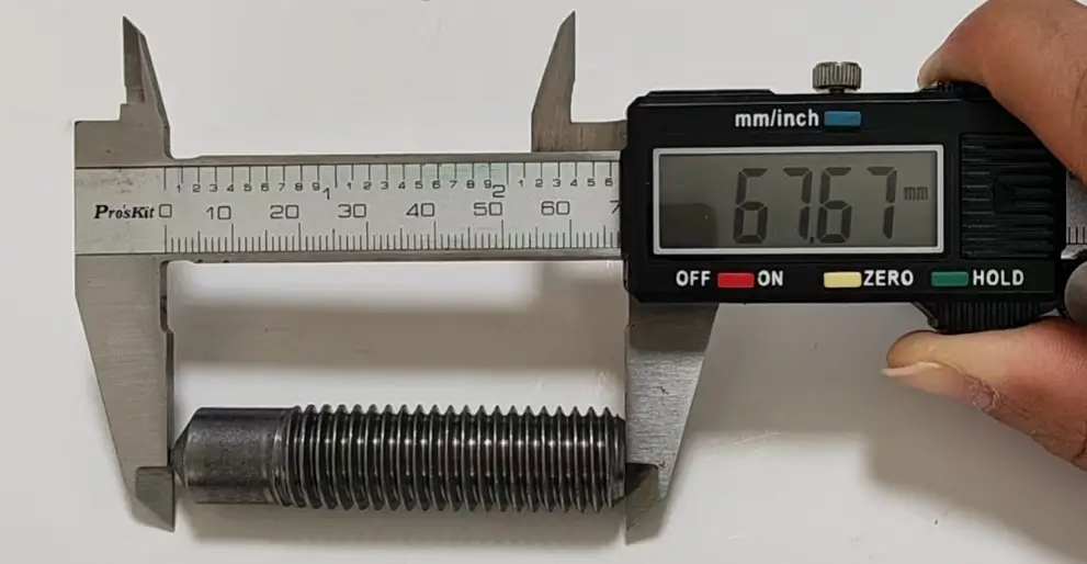 Digital caliper measuring a threaded arc welding stud showing 67.67mm length for quality control.