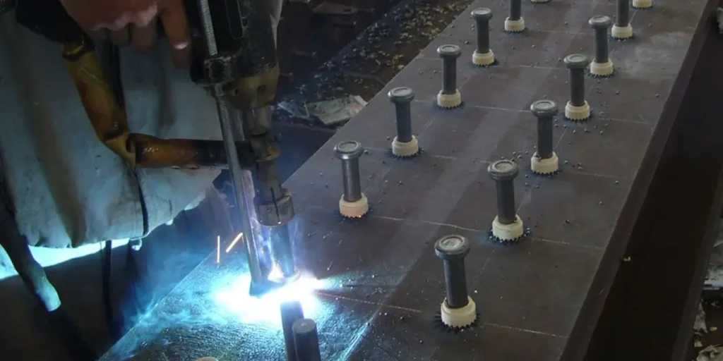 Industrial drawn arc stud welding machine installing shear connectors on an H-beam at a steel structure construction site.