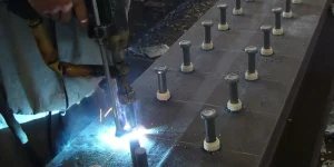 Industrial drawn arc stud welding machine installing shear connectors on an H-beam at a steel structure construction site.