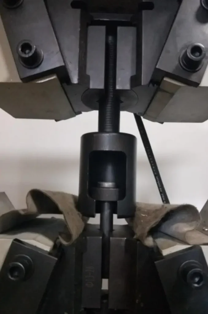 Universal testing machine conducting a tensile strength test on a shear stud for quality inspection.