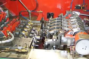 Automatic multi-station cold heading machine forging metal wire into weld stud blanks.